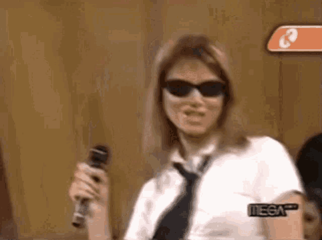 a woman in sunglasses and a tie is holding a microphone .