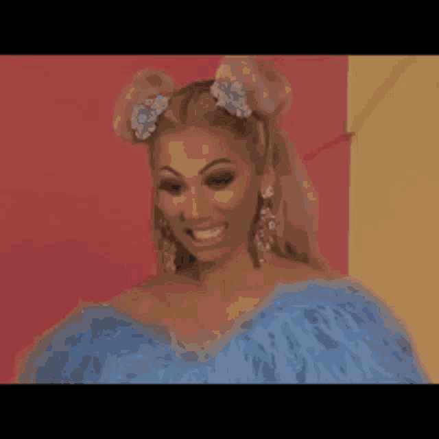 a woman is wearing a blue feathered dress and earrings and smiling .