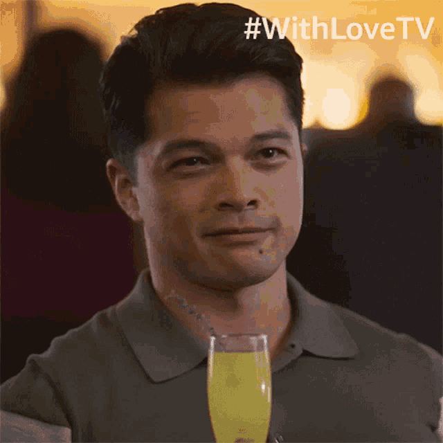 a man holding a glass of yellow liquid with #withlovetv on the bottom right