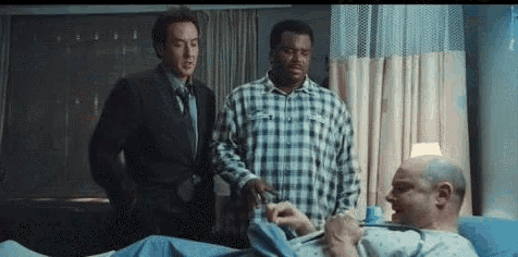 two men are standing next to a man in a hospital bed