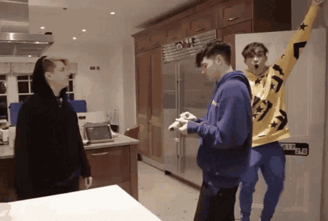 a man in a yellow converse sweatshirt stands in a kitchen with two other men