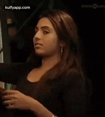 a woman in a black dress is making a funny face while sitting in a dark room .
