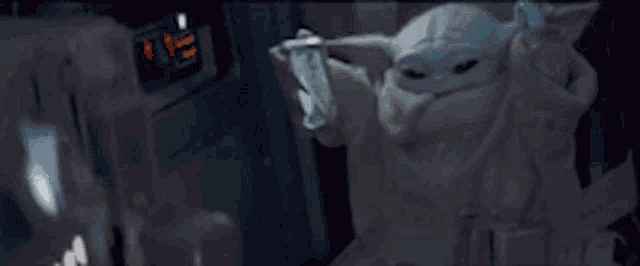 a baby yoda is sitting in a chair holding a can of soda and giving the middle finger .