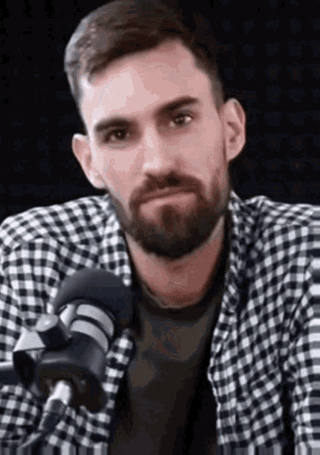 a man with a beard wearing a plaid shirt is talking into a microphone