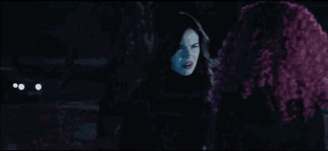 a woman with pink curly hair is standing next to a man in a dark room .