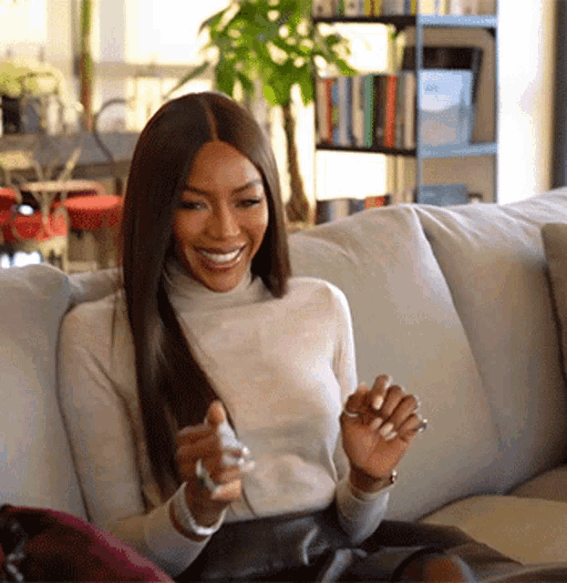 a woman is sitting on a couch smiling and holding her hand up