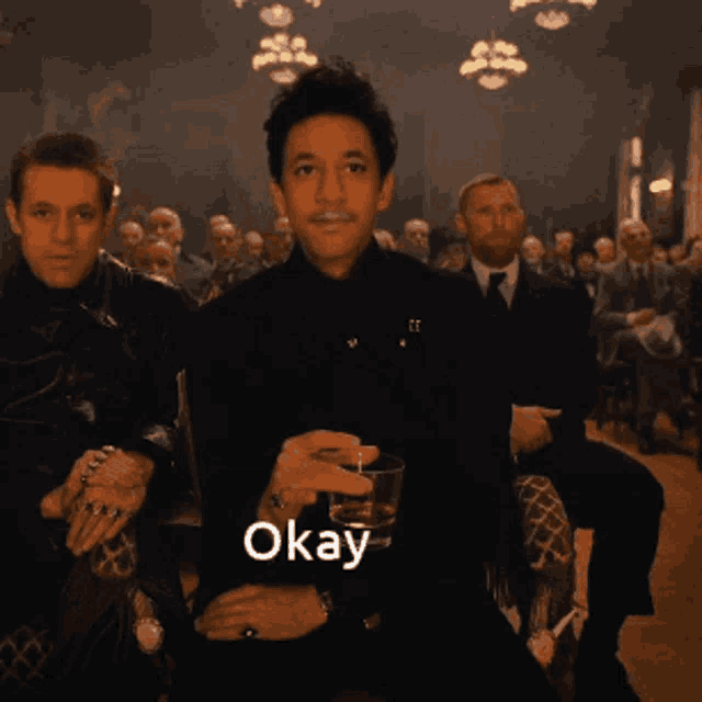 a man sitting in a crowd holding a glass with the word okay written on it