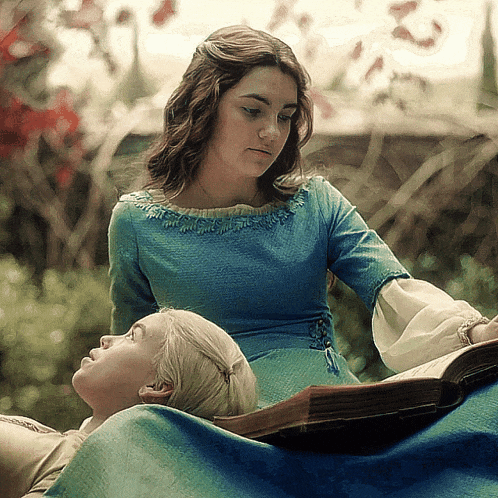 a woman in a blue dress is reading a book to another woman in a blue dress