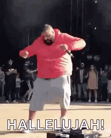 a man in a red hoodie and white shorts is dancing on a stage while holding a microphone in his hand .