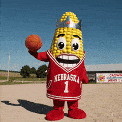 a corn on the cob mascot holding a basketball and wearing a nebraska jersey