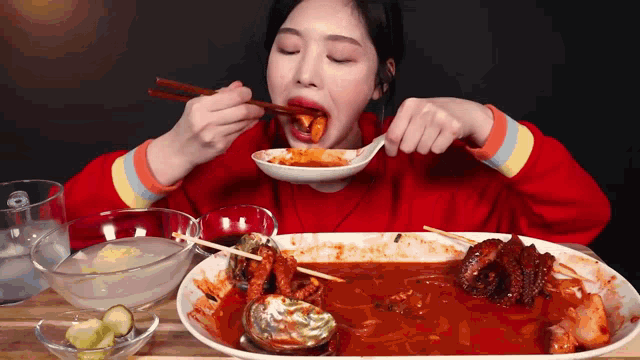a woman in a red sweater is eating food with chopsticks