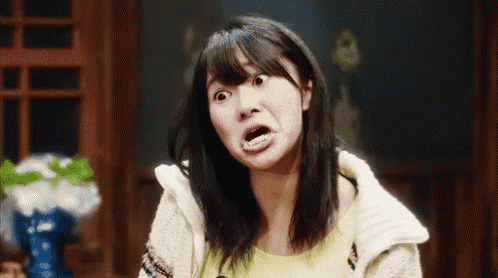 a woman is making a funny face with her mouth open and a vase of flowers in the background .