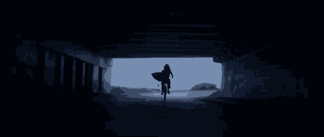 a person riding a bike in a dark tunnel with a surfboard