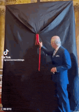 a man in a suit is holding a red ribbon in front of a black cloth .