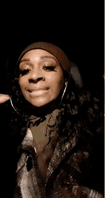 a woman wearing a beanie and a jacket is making a funny face while holding her hand to her face .