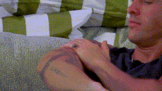 a man with a tattoo on his arm is sitting on a couch with striped pillows