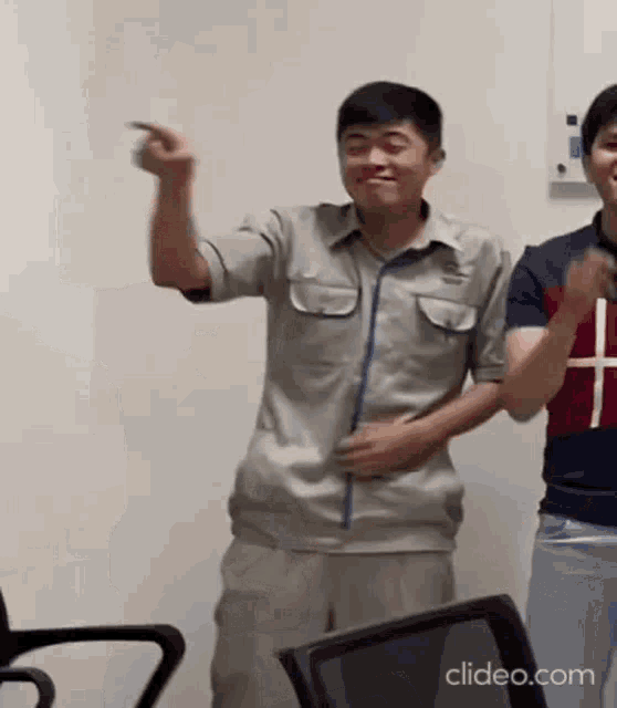 a man in a gray shirt is dancing in a room while another man looks on .