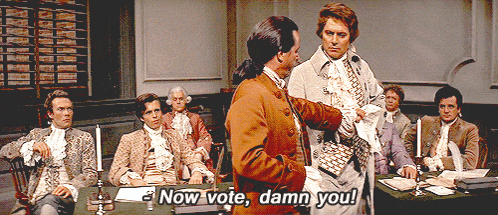 a group of men are sitting around a table and one of them is saying now vote damn you