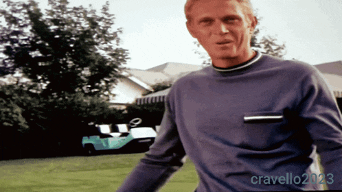 a man in a blue sweater is standing in a grassy yard with a picture of him taken by cravello2123