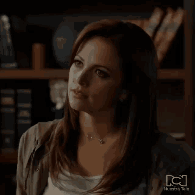 a woman is sitting in front of a bookshelf and making a face .