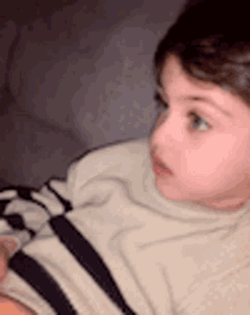 a young boy is laying on a couch wearing a striped sweater .