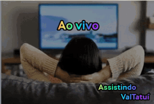 a woman is sitting on a couch watching a tv screen that says ao vivo assistindo valtatui on it