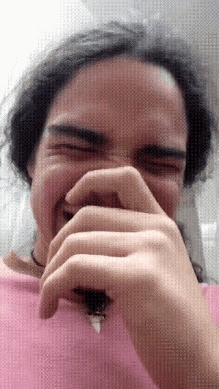 a man in a pink shirt is covering his mouth with his hands