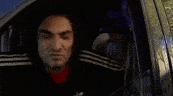 a man wearing a black and white adidas jacket is giving the middle finger while sitting in a car .