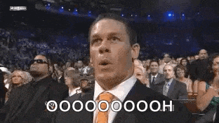 a man in a suit and tie is making a surprised face while sitting in front of a crowd .