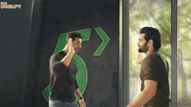 two men are standing next to each other in front of a green sign that says 5