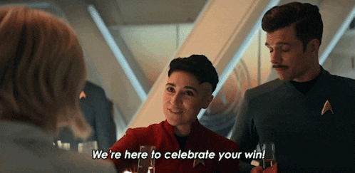 a man and a woman are sitting at a table and the man is saying we 're here to celebrate your win