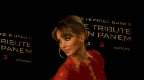 a woman in a red dress is smiling in front of a sign that says die tribute von panem