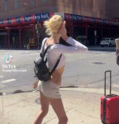 a woman with a backpack is walking down a street with a suitcase in front of a building that says legendary hall
