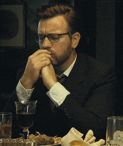 a man wearing glasses sits at a table with a glass of wine in front of him