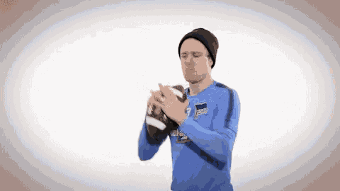a man in a blue shirt and black hat is holding a football .