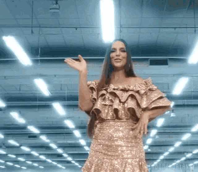 a woman in a gold dress is dancing in a warehouse