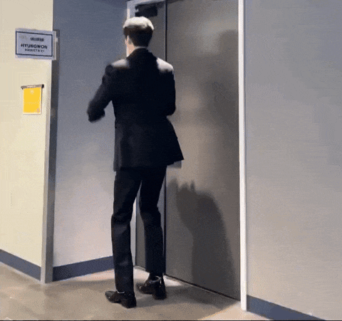 a man in a suit is standing in front of a door with a sign that says hyuwon