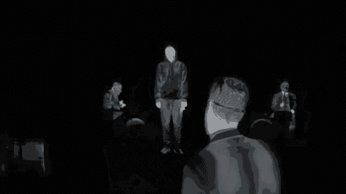 a group of people standing in a dark room including a man in a suit and tie
