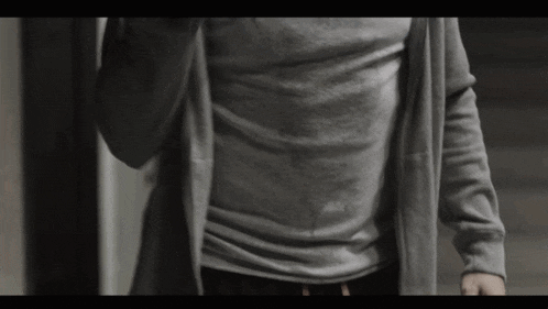 a man wearing a grey shirt and a grey cardigan is walking down stairs
