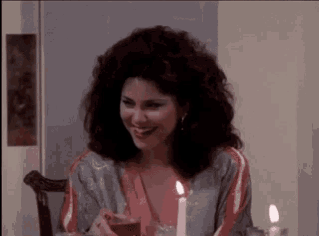 a woman is sitting at a table with a candle and a drink .