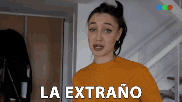 a woman in a yellow sweater is standing in front of a sign that says la extrano