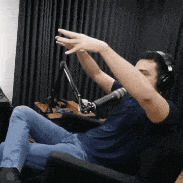 a man wearing headphones is sitting in front of a microphone with his hands in the air