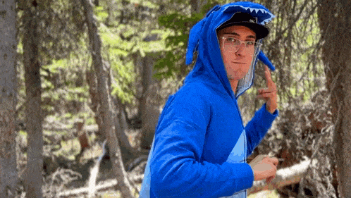 a man in a blue shark costume is standing in the woods