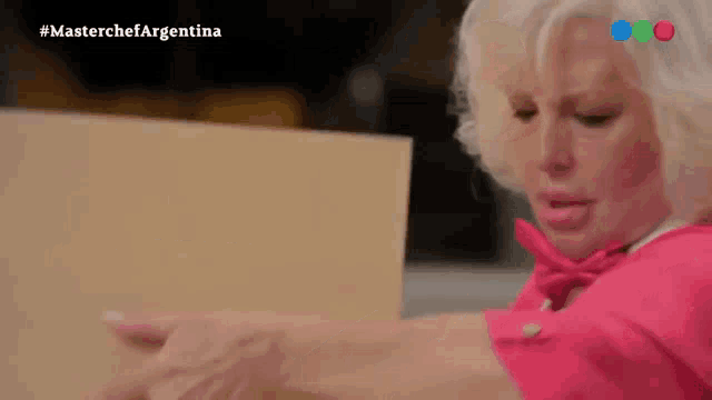 a woman in a pink shirt is holding a piece of paper in front of a screen that says master chef argentina
