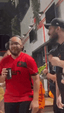 a group of men are standing next to each other in a room . one of the men is wearing a red shirt .
