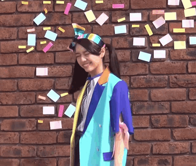 a woman stands in front of a brick wall with sticky notes falling from the sky
