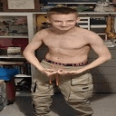 a shirtless young man in khaki pants is standing in front of a shelf .
