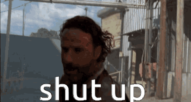 a man with a beard is standing in front of a building with the words shut up written on it