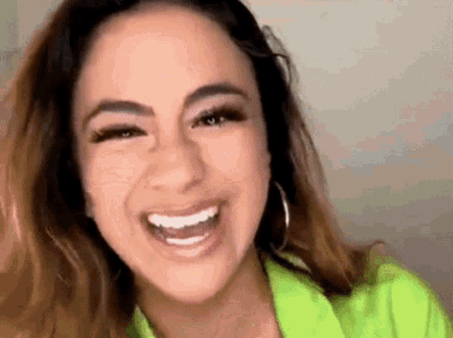 a close up of a woman laughing with her mouth open and wearing a green jacket .