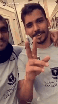 two men are standing next to each other and giving a peace sign .